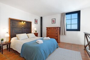 Un dormitorio con cama, cómoda, mesita de noche, lámpara y ventana con cortinas.