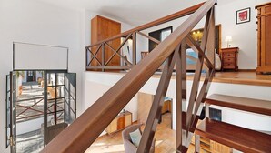 Een trap met houten leuningen, een uitzicht op het interieur met een bank en een kast, en een deur die naar buiten leidt.