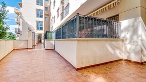Un couloir au sol carrelé, une balustrade de balcon en métal et la façade d’un immeuble dotée de nombreuses fenêtres et de balcons.