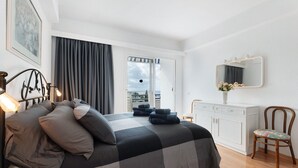 Ein Schlafzimmer mit einem Bett, einem Schminktisch, einem Sessel, einem Fenster mit Vorhängen und einer zur Außenwelt führenden Tür.
