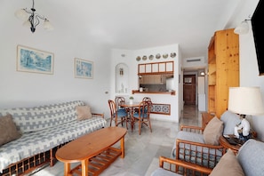 A living room with a sofa, wooden coffee table, and chairs, a dining area with a table and chairs, and a kitchen visible through an archway. - Vacation Home "Club Atlantis with Views" with Shared Pool & Wi-Fi (Costa Adeje)