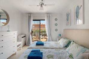 Une chambre à coucher comprenant un lit, une commode, un ventilateur de plafond, une fenêtre avec des rideaux et un balcon.