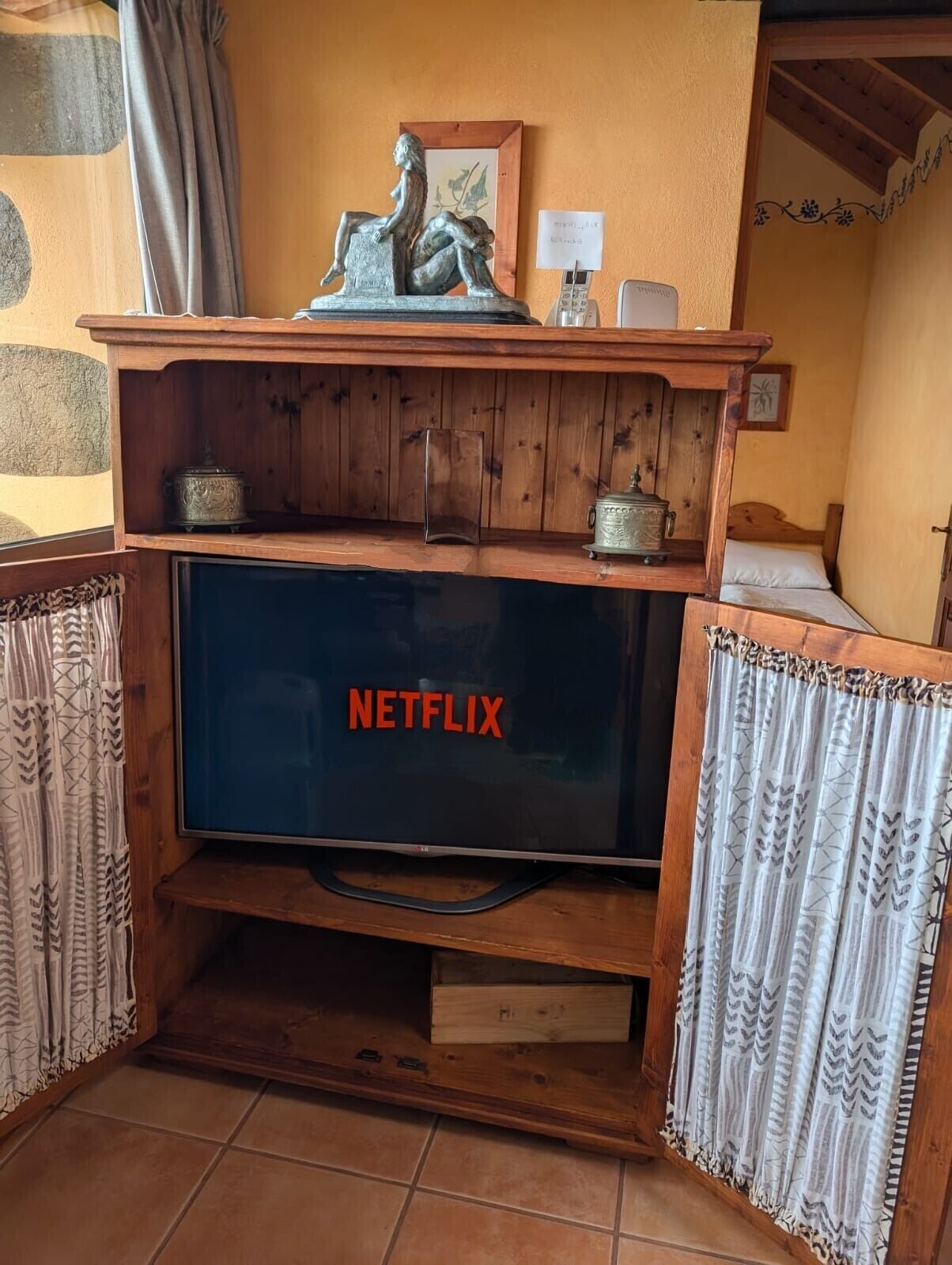 A wooden TV stand with a Netflix logo, a small statue, and a framed picture on top.