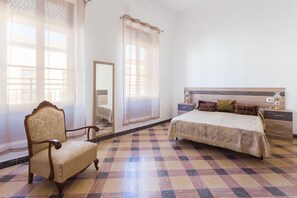 Ein Schlafzimmer mit kariertem Boden, einem Bett mit Kopfteil, einem Stuhl, einem Nachttisch und einem Spiegel.