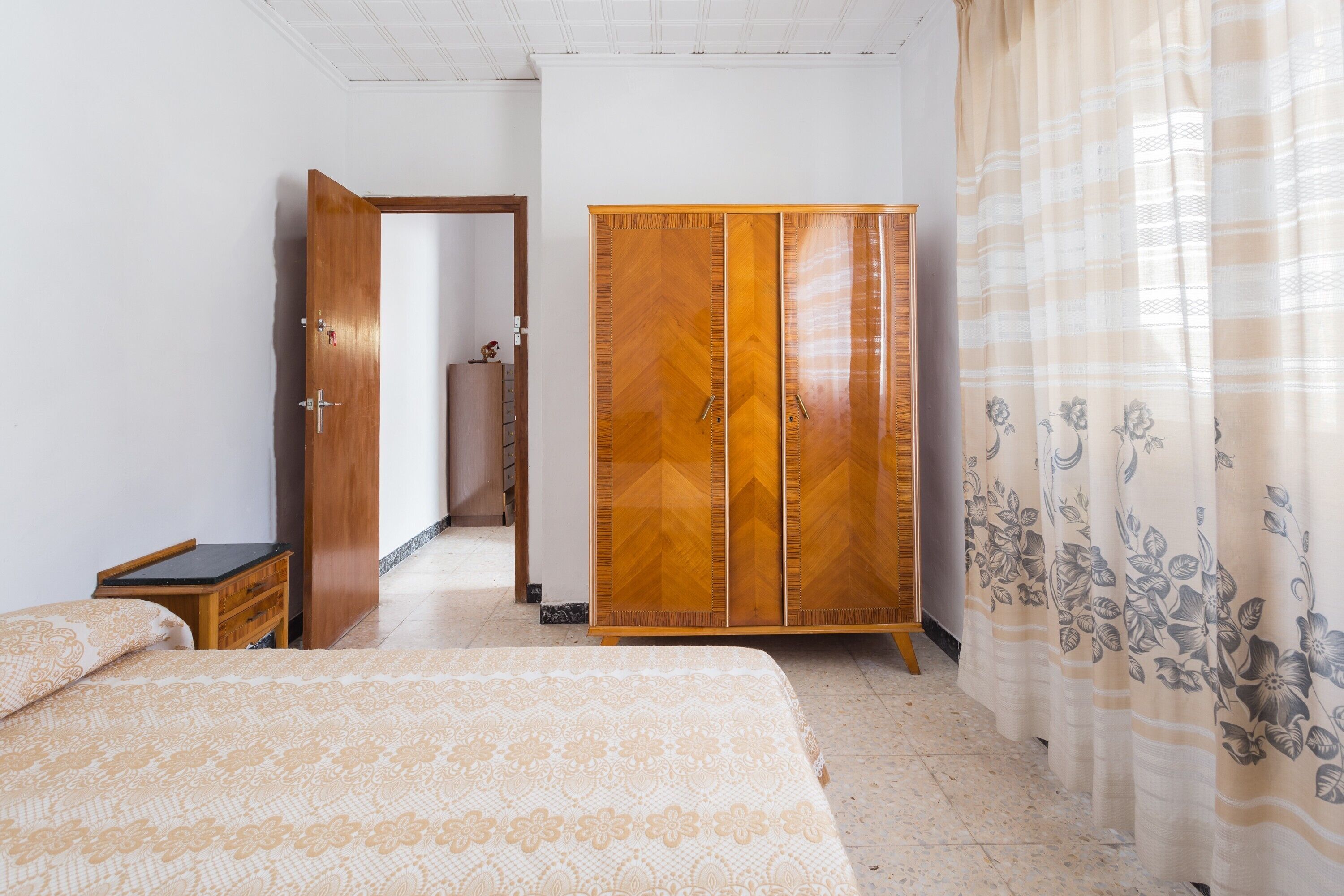 Un dormitorio con cama, armario, mesita de noche y puerta que da a otra habitación.