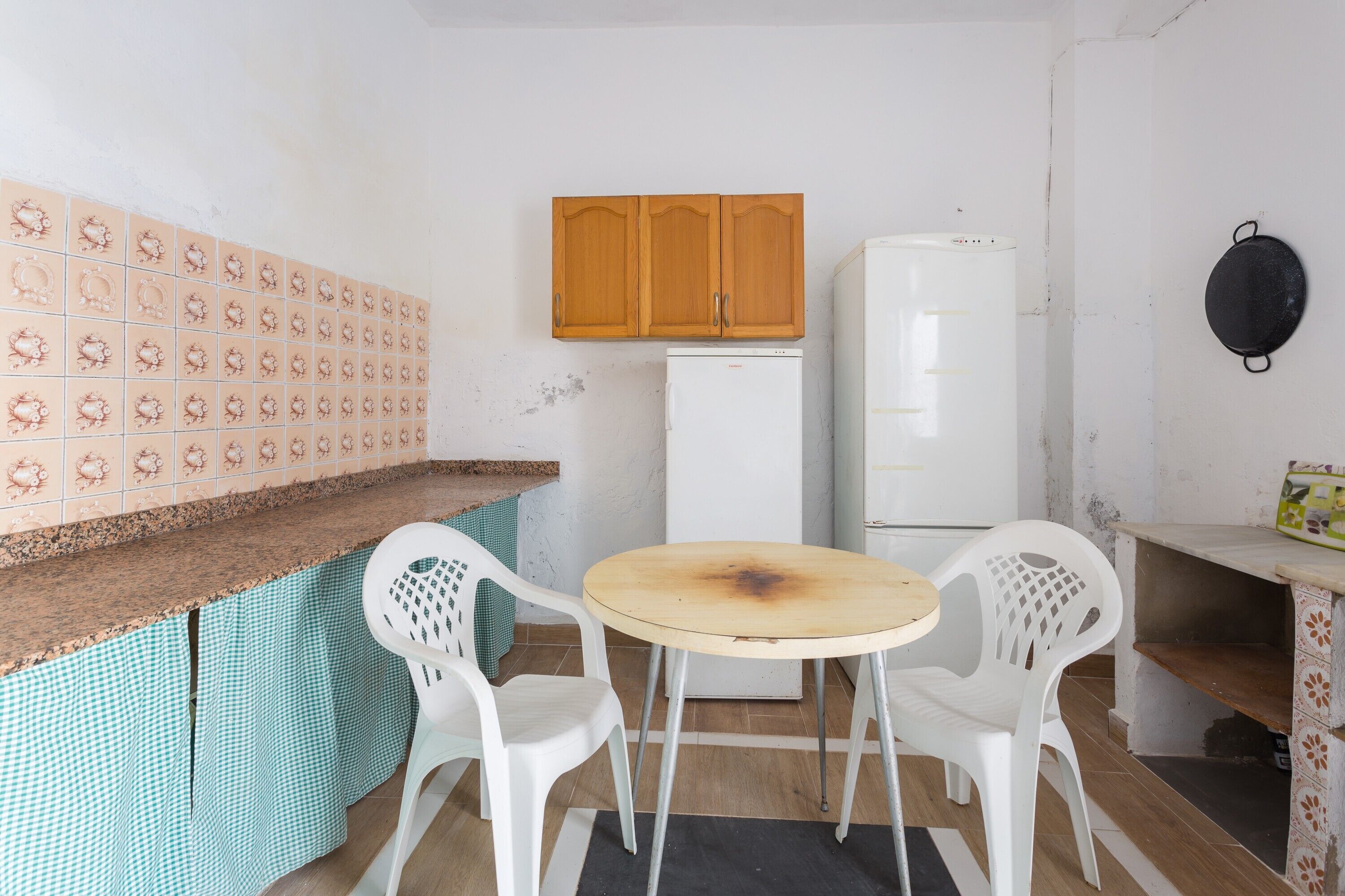 Una piccola cucina con frigorifero, un armadietto in legno, un tavolo rotondo e due sedie bianche.