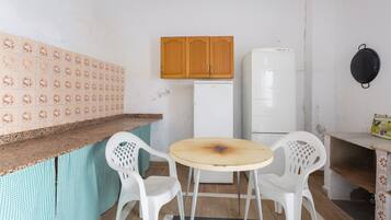 Una piccola cucina con frigorifero, un armadietto in legno, un tavolo rotondo e due sedie bianche.