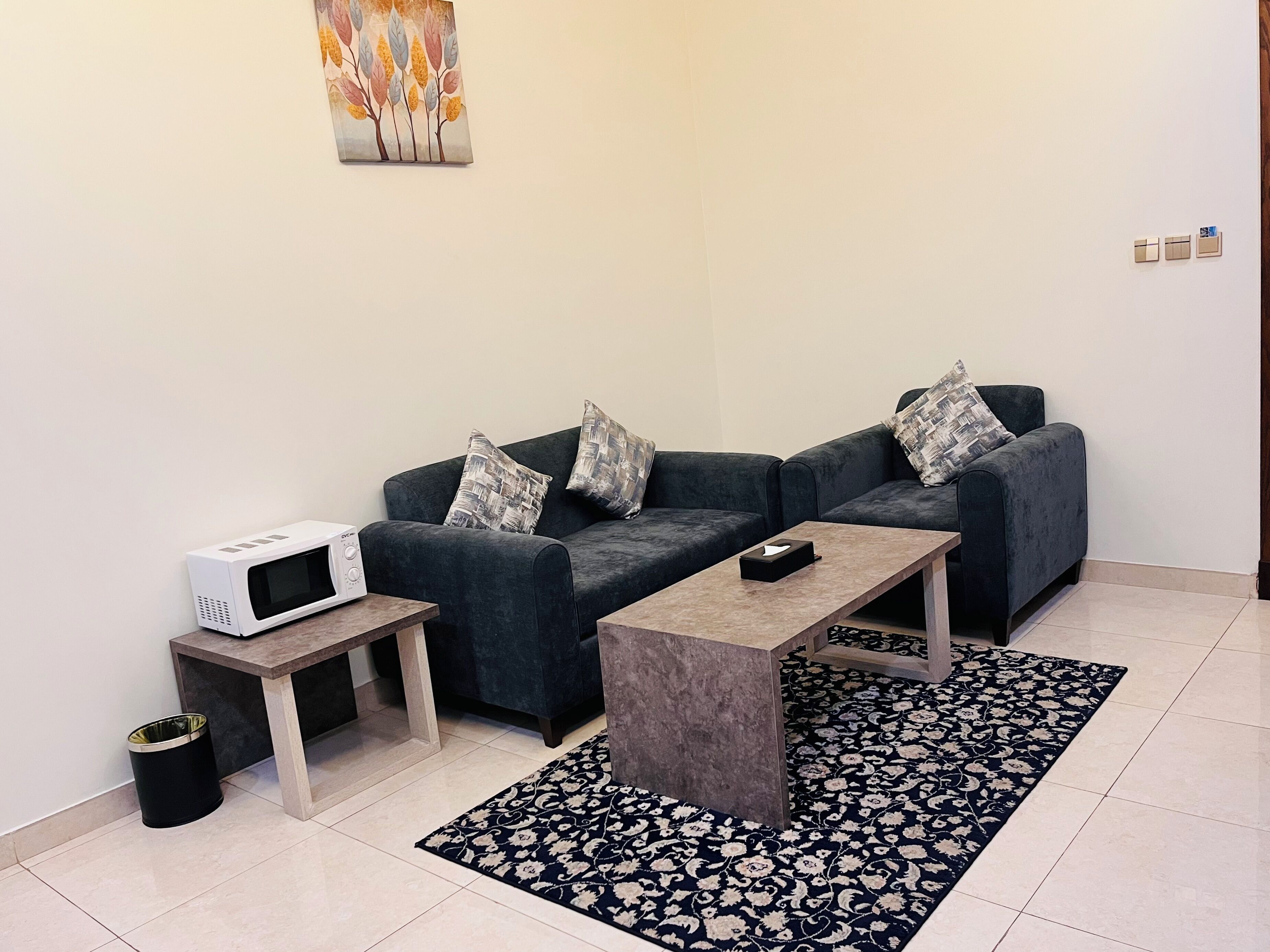 A modern living room with a grey sofa set, a coffee table, a microwave, and a patterned rug.