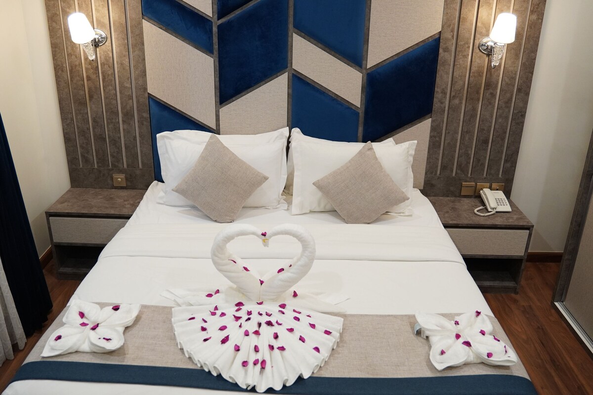 Ein Hotelzimmer mit einem Bett, zwei Nachttischen, einem Telefon und einer dekorativen Schwaneinrichtung.