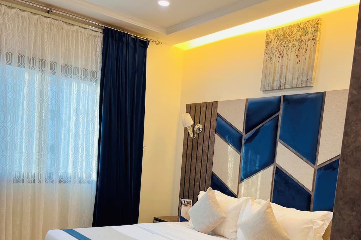 A modern hotel room with a large bed, wooden flooring, and a decorative headboard.