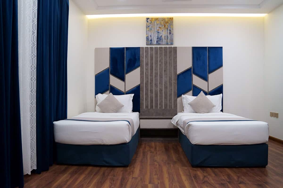 A hotel room with two beds, a wooden floor, and a geometric wall art piece.