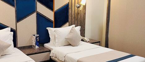 A hotel room with two beds, a wooden headboard, a painting, a nightstand, and a wall-mounted lamp.