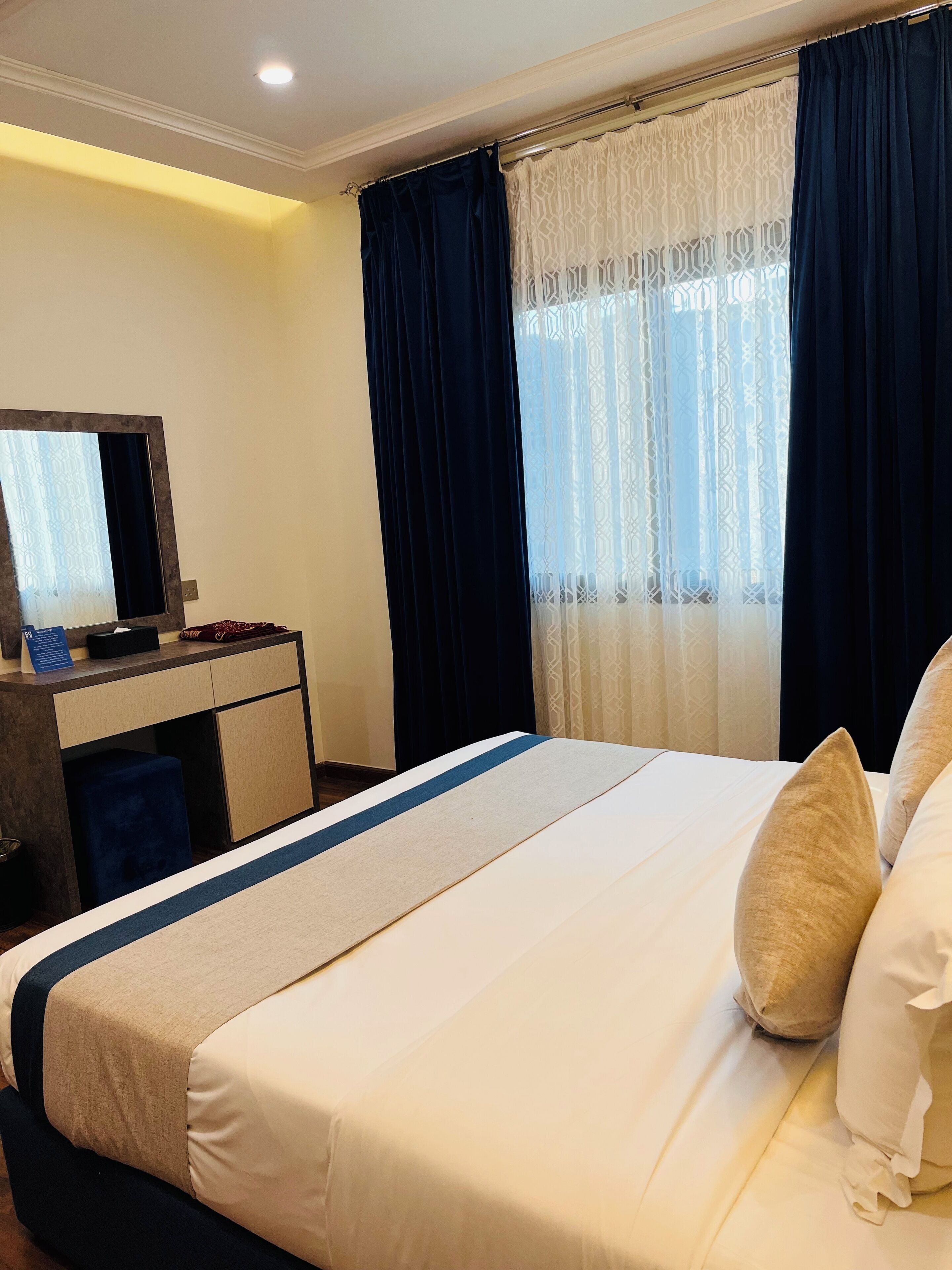 A hotel room with a bed, a desk with a computer, and a window with curtains.