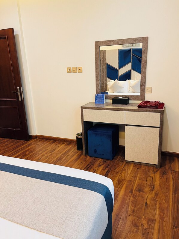 A hotel room with a bed, a desk with a mirror, and a blue storage bin. - Mabeet Al-Khobar Served Apartment (Al Khobar)