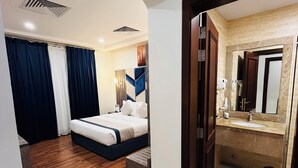 Una camera d'albergo con un letto, un bagno con lavandino e specchio, e un pavimento in legno.