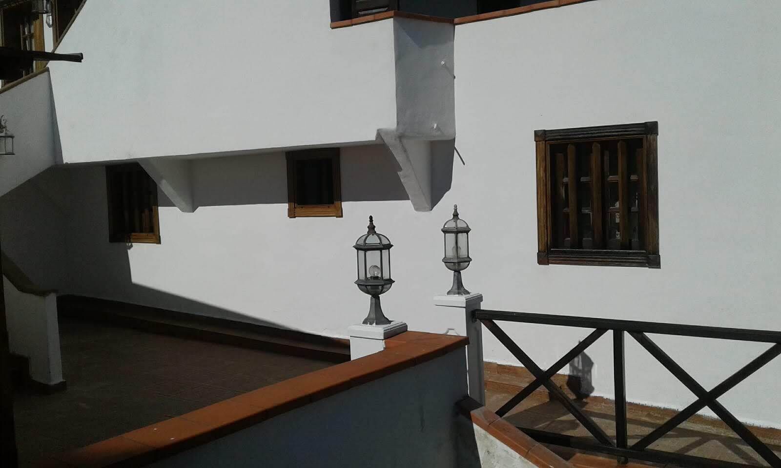 Un bâtiment blanc doté d’un balcon, de deux lampes de style lanterne et d’une fenêtre avec des barreaux verticaux.