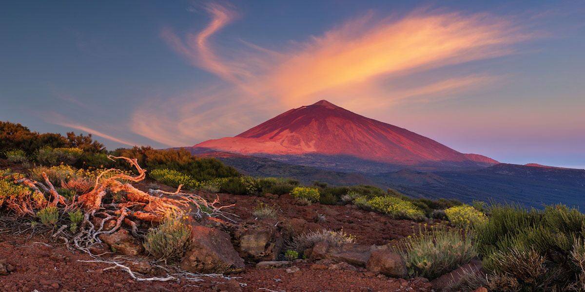 Paisaje volcánico con una montaña destacada, terreno rocoso y vegetación escasa.