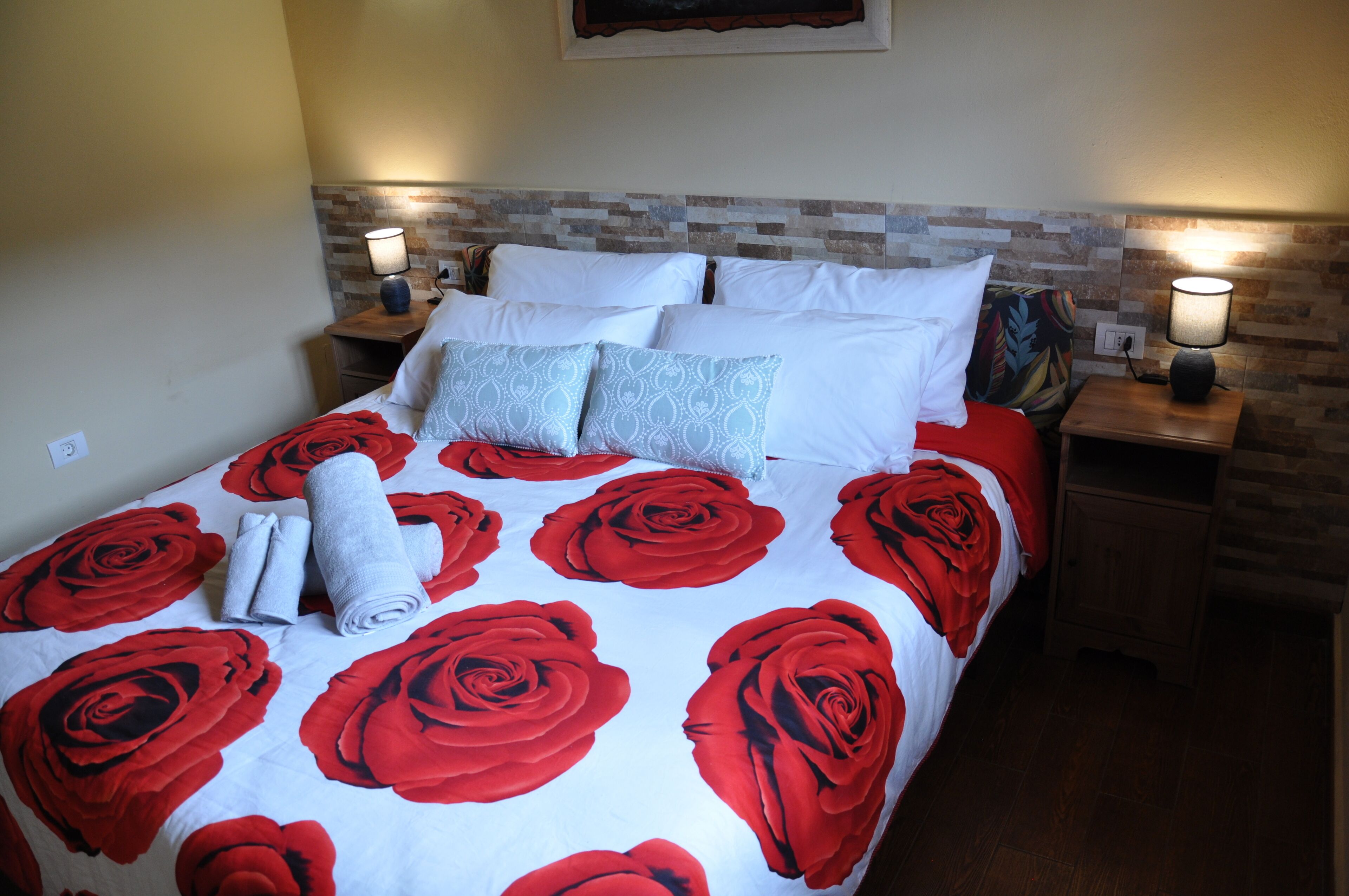 A bed with a red and white rose pattern, two bedside lamps, and a wooden headboard.