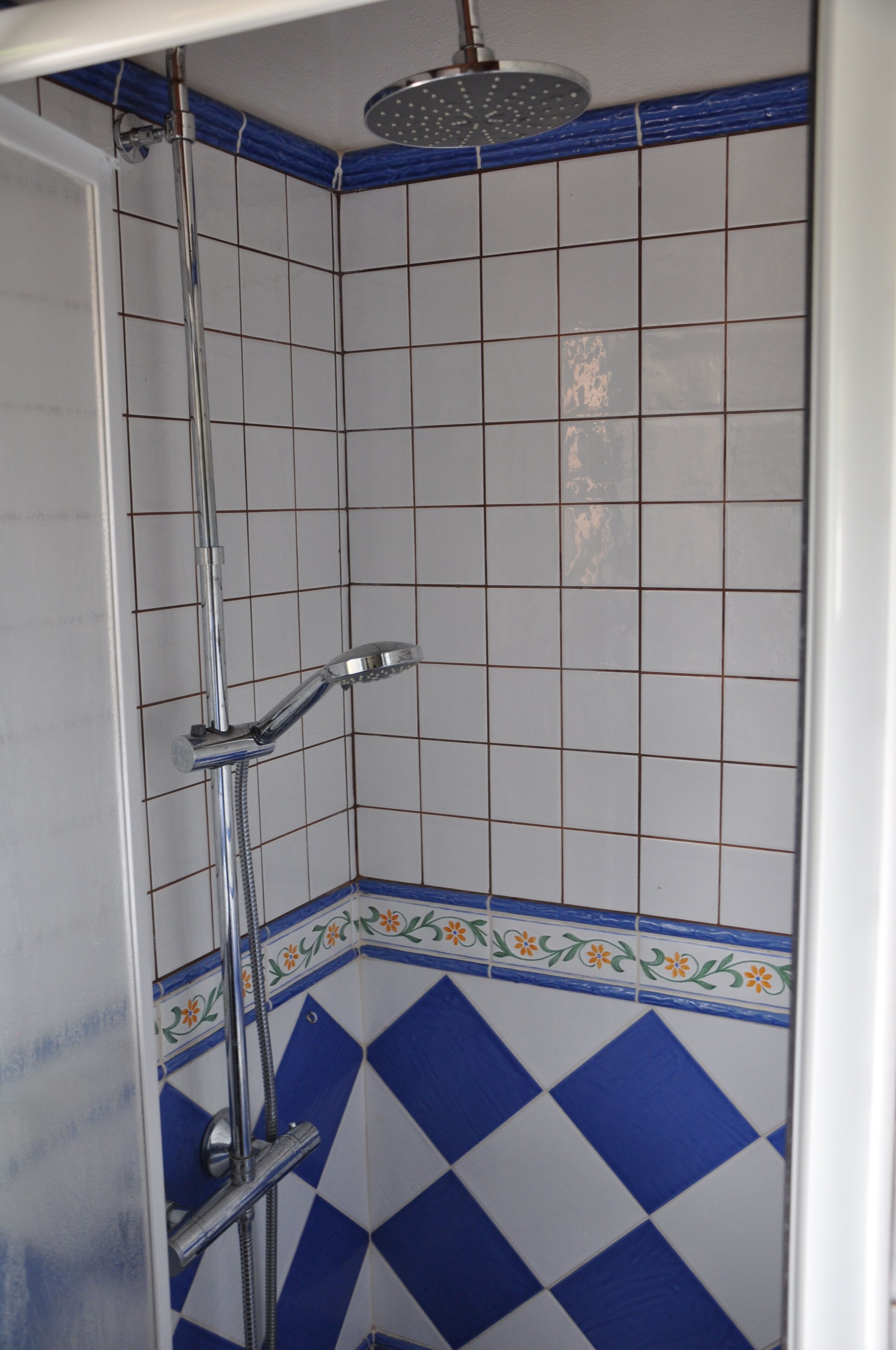 A shower with a chrome fixture and a blue and white tiled wall.