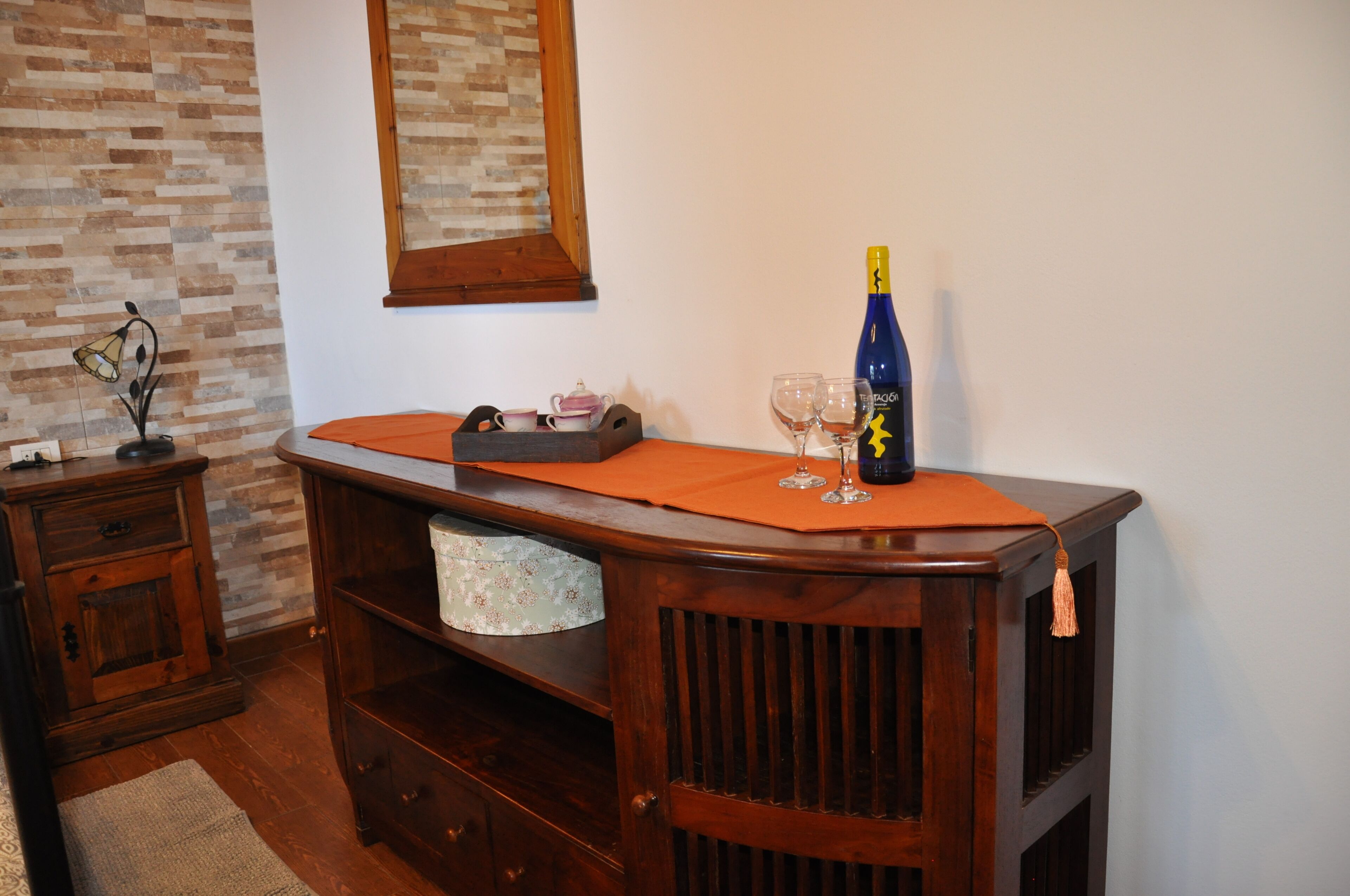 Un aparador de madera con una botella, vasos y una tetera.