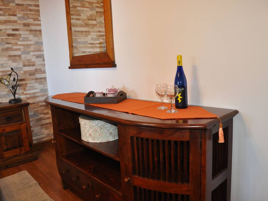 Un aparador de madera con una botella, vasos y una tetera.