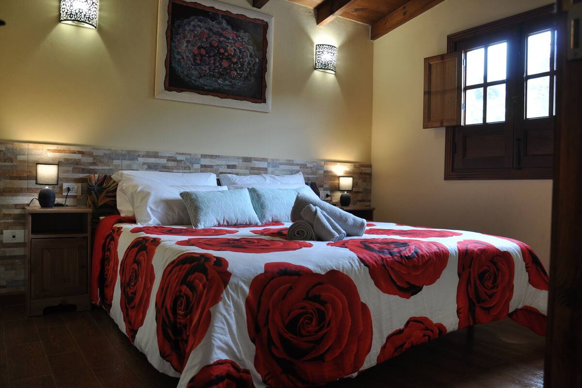 Een slaapkamer met een groot bed, een houten hoofdbord, een schilderij aan de muur en twee wandlampen.
