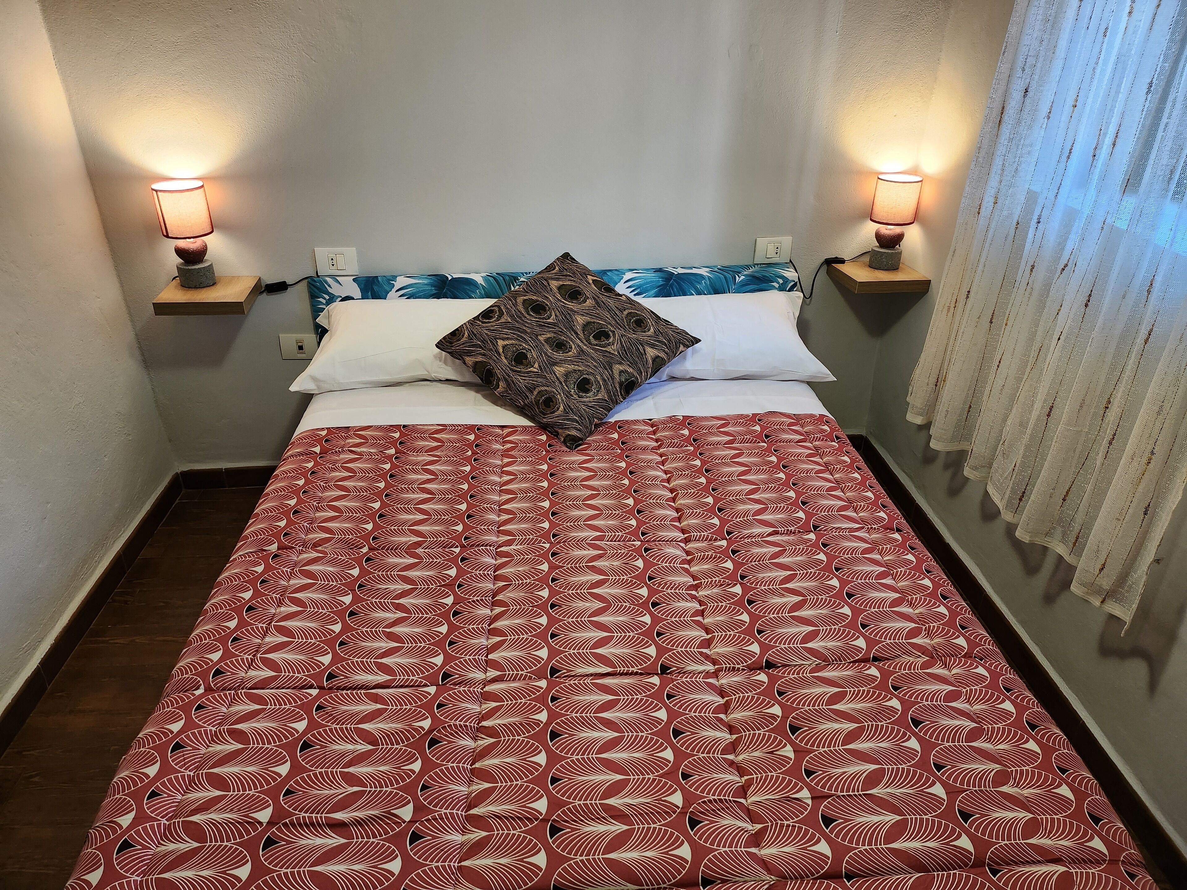 A neatly made bed with a patterned bedspread, two bedside lamps, and a pillow with a peacock design.