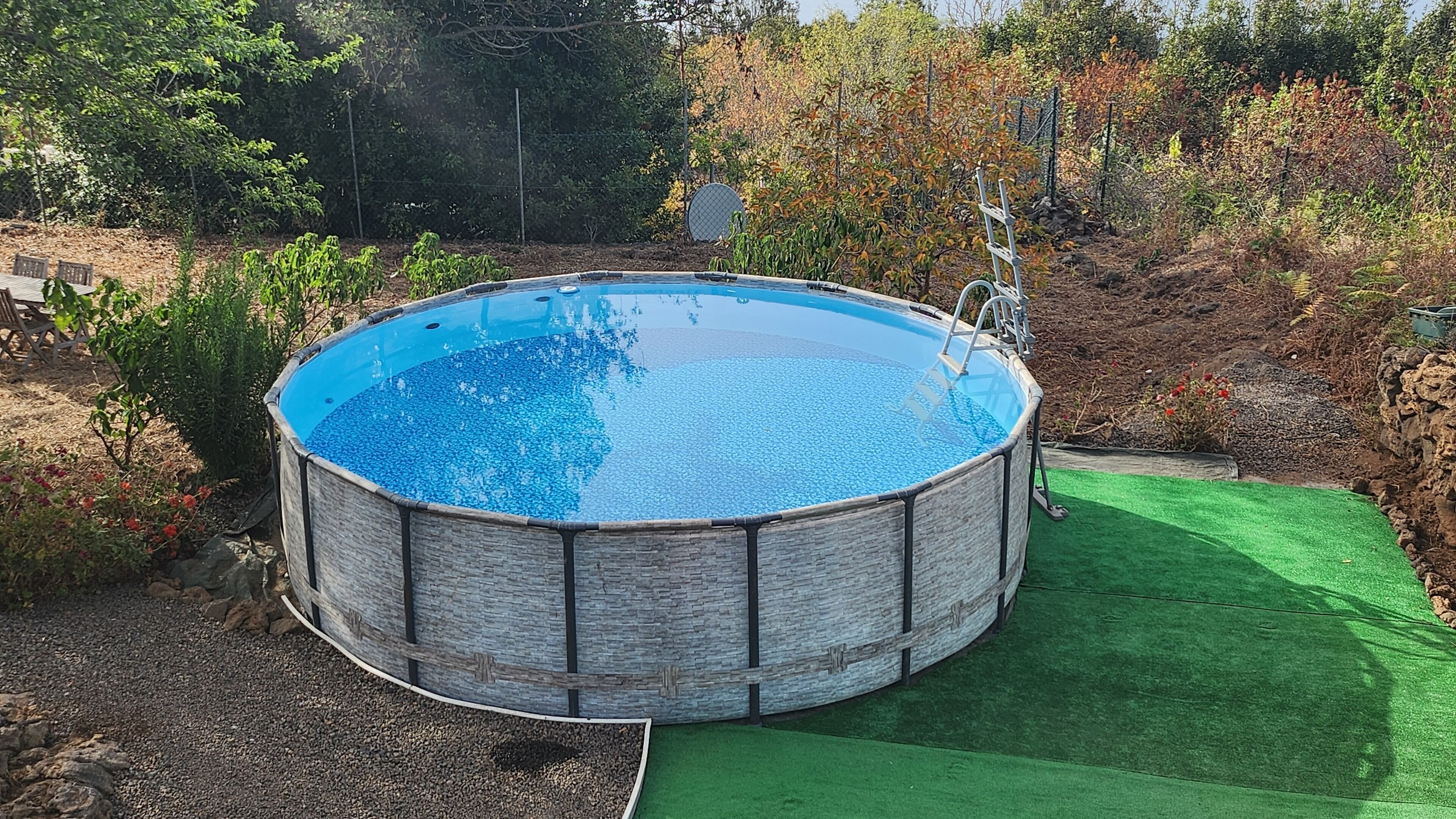 A round above-ground pool with a ladder, surrounded by a green artificial turf and gravel.