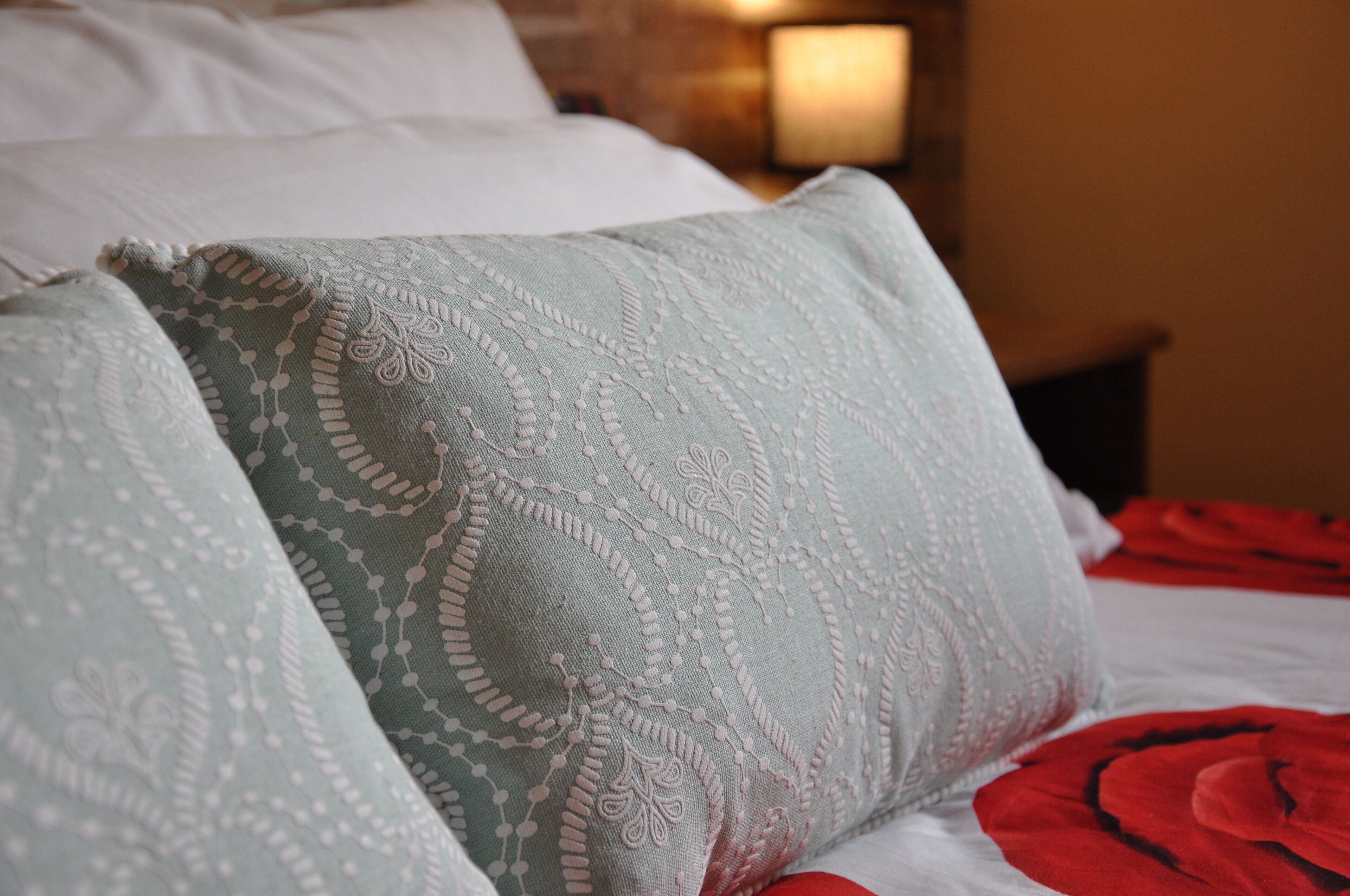 A bed with patterned pillows and a red blanket.