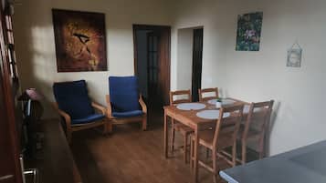 Un coin repas avec une table et des chaises en bois, un tableau accroché au mur et une porte donnant sur une autre pièce.