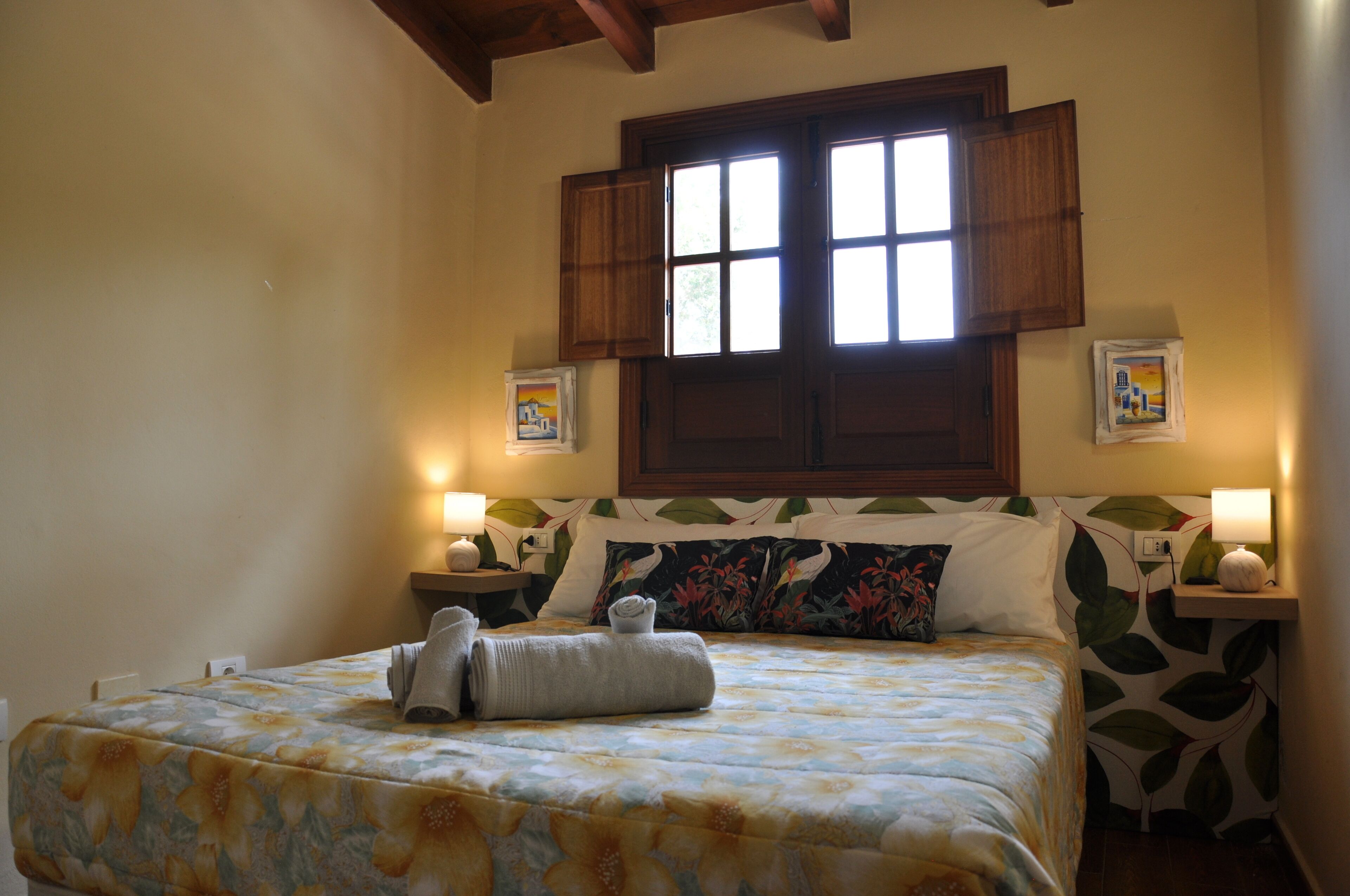 Una cama bien hecha con toallas, una ventana con contraventanas y una pared con un diseño de hojas.