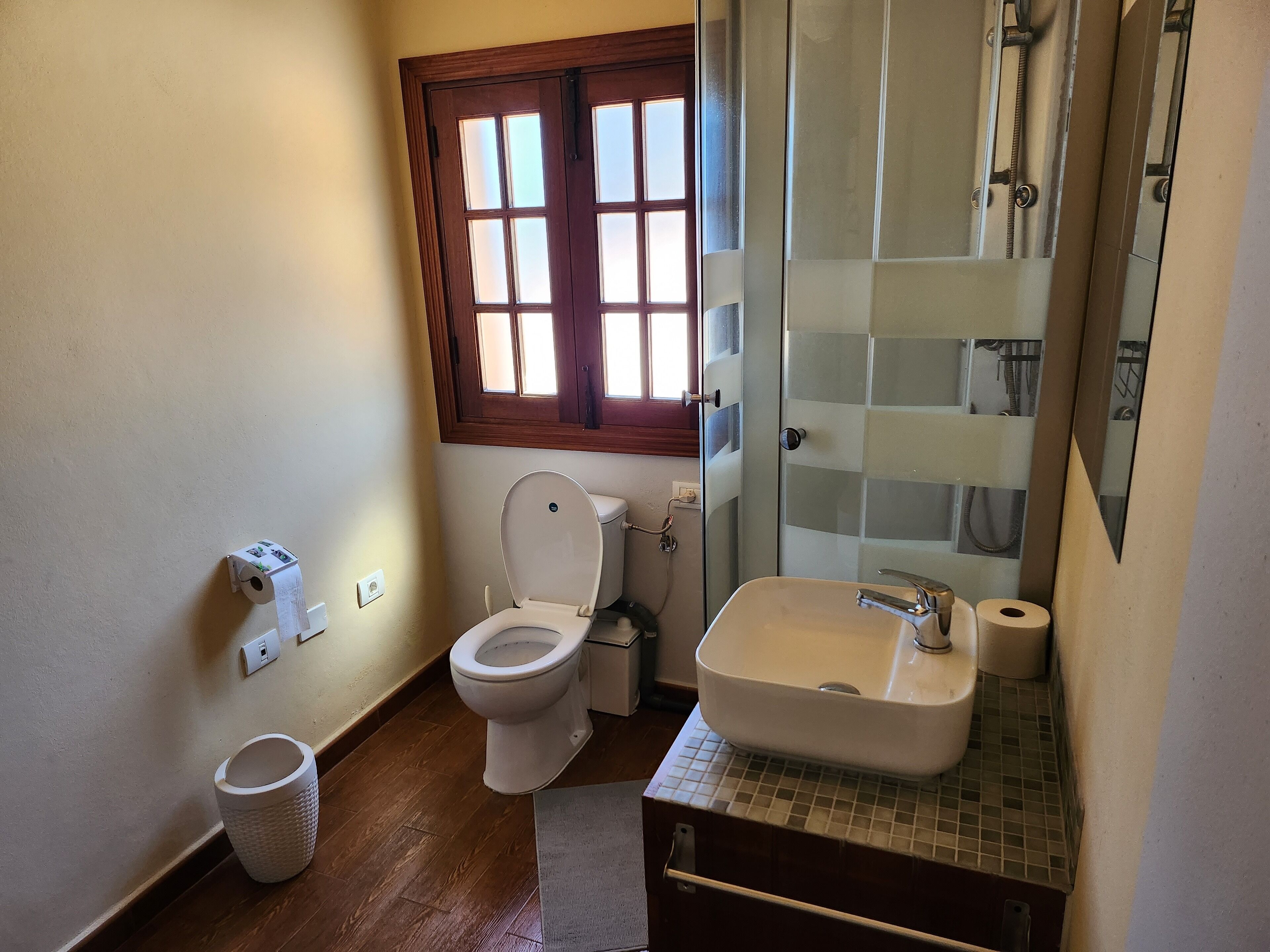 A bathroom with a toilet, sink, and a window above the toilet.