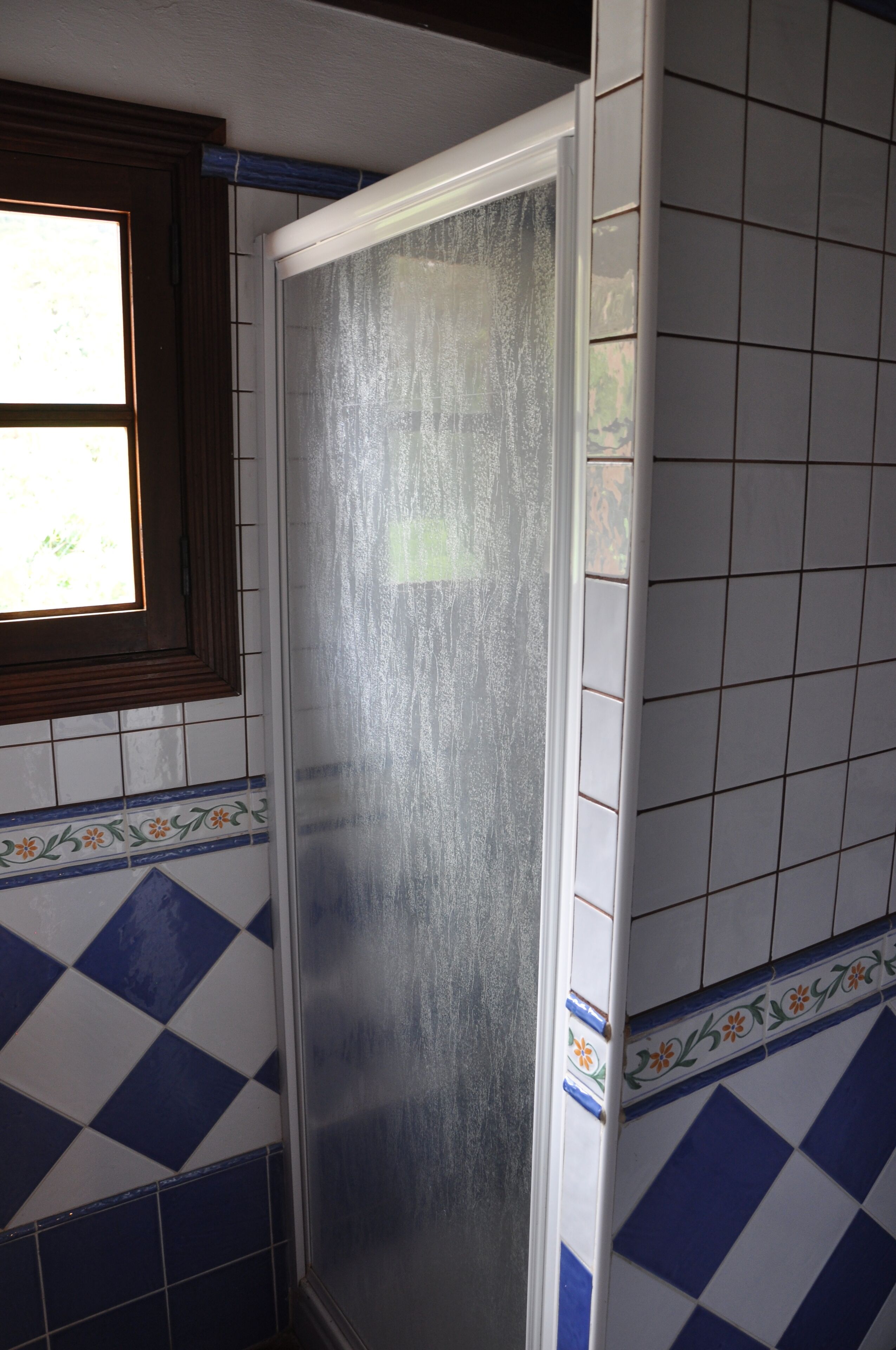 Un baño con cabina de ducha, paredes con azulejos y una ventana.