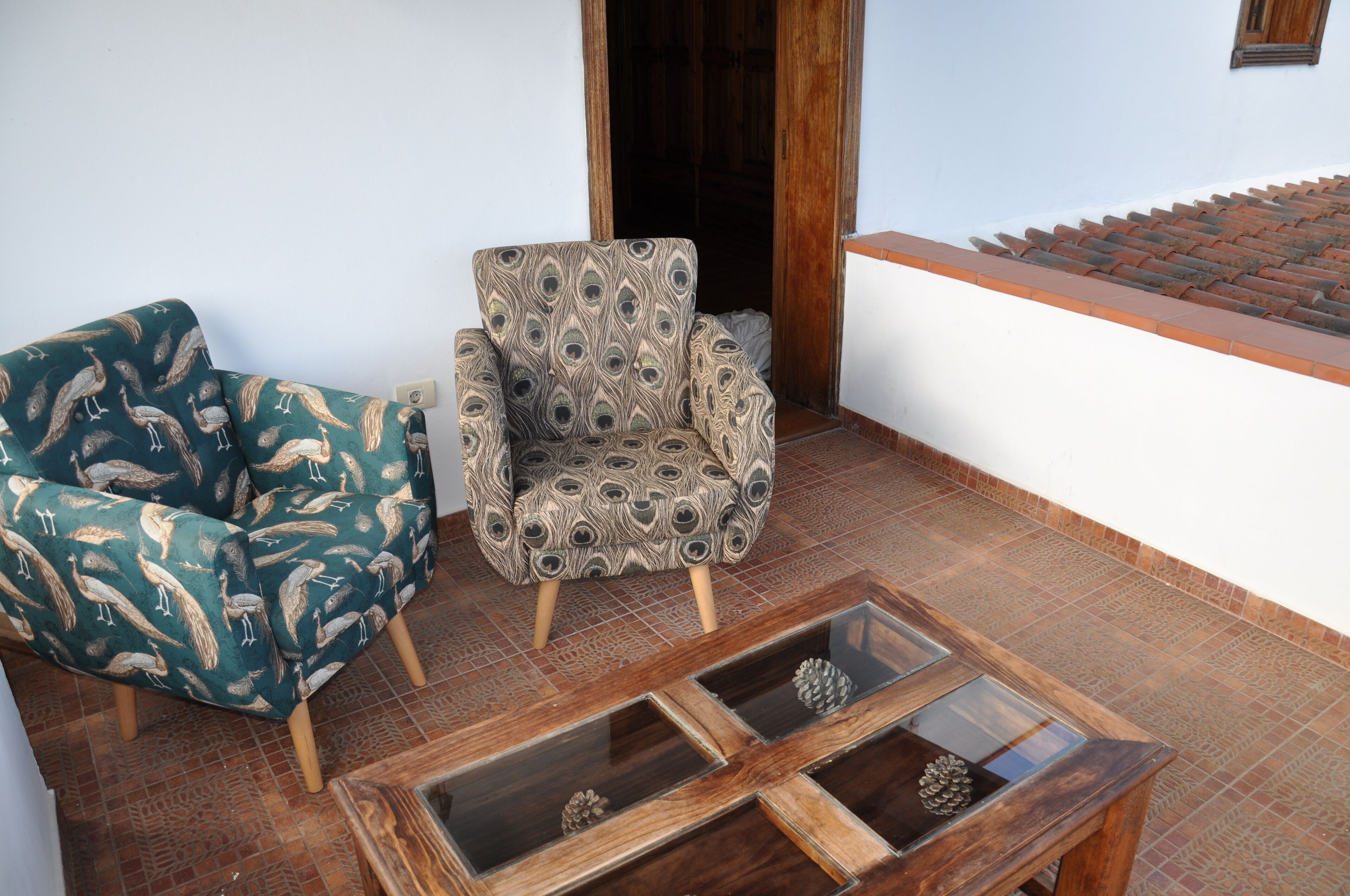 A room with a patterned armchair, a wooden coffee table with glass panels, and a tiled floor.