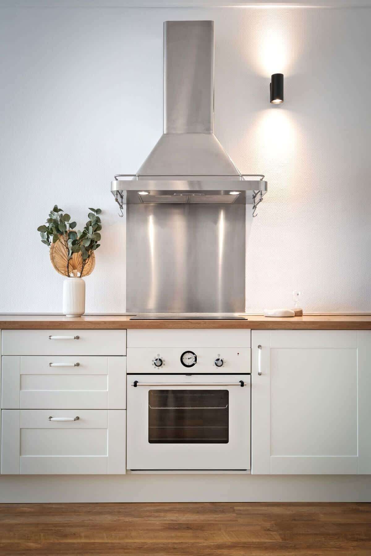 A kitchen with a stainless steel range hood, a built-in oven, and a wall-mounted light fixture.