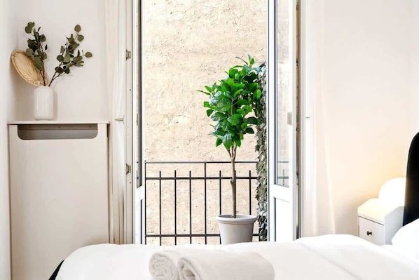 Une chambre d’hôtel avec un lit, une plante en pot, un petit balcon avec une balustrade et une fenêtre.