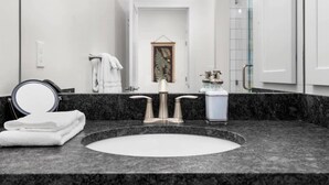 Ein Badezimmer mit einem runden Waschbecken, einem Spiegel, einem Handtuch und einem gerahmten Bild an der Wand.