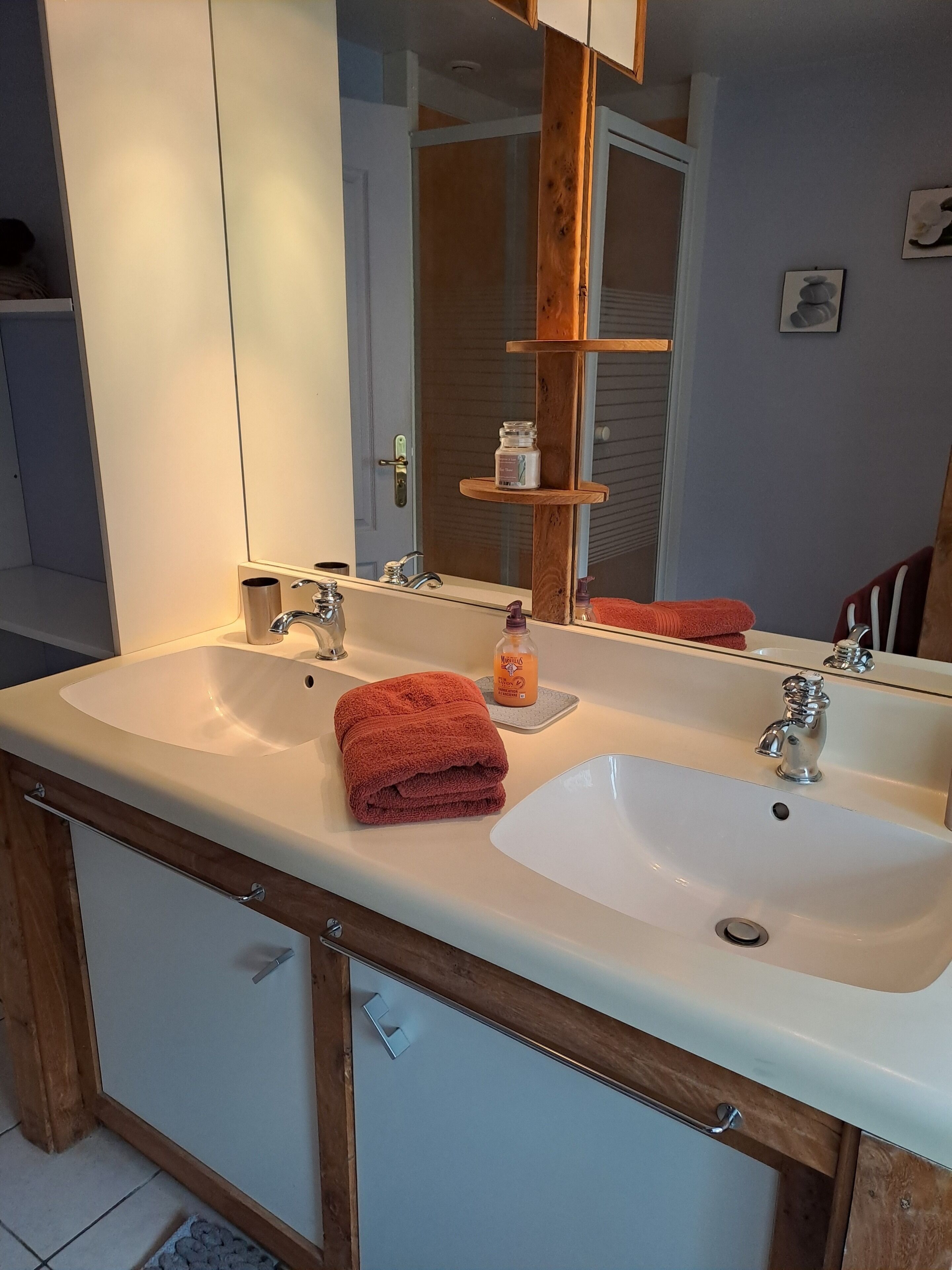 A bathroom with a double sink, wooden cabinets, a mirror, and a towel rack.