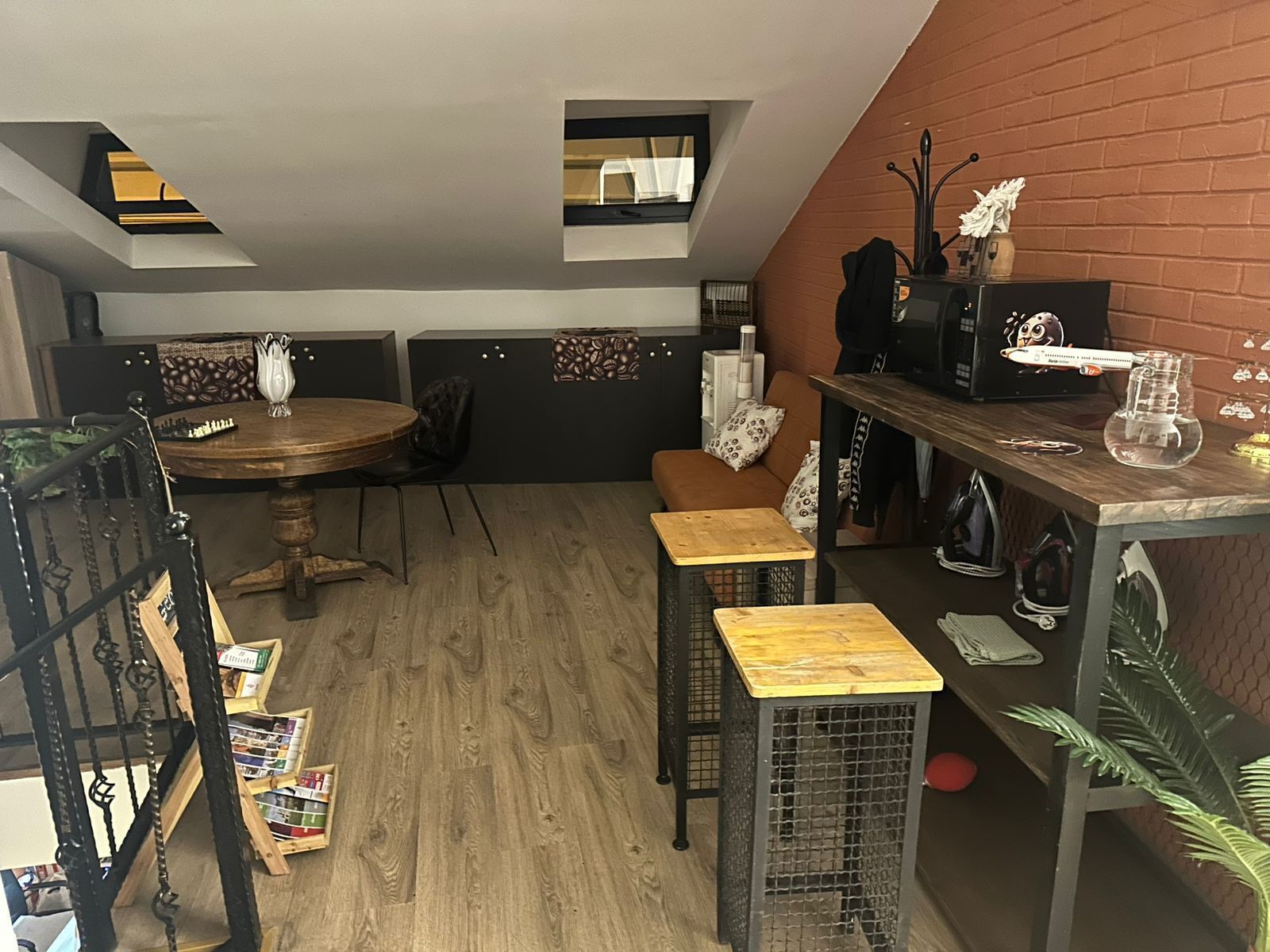 A cozy room with a dining table, bar stools, a small kitchen area, and a brick wall.
