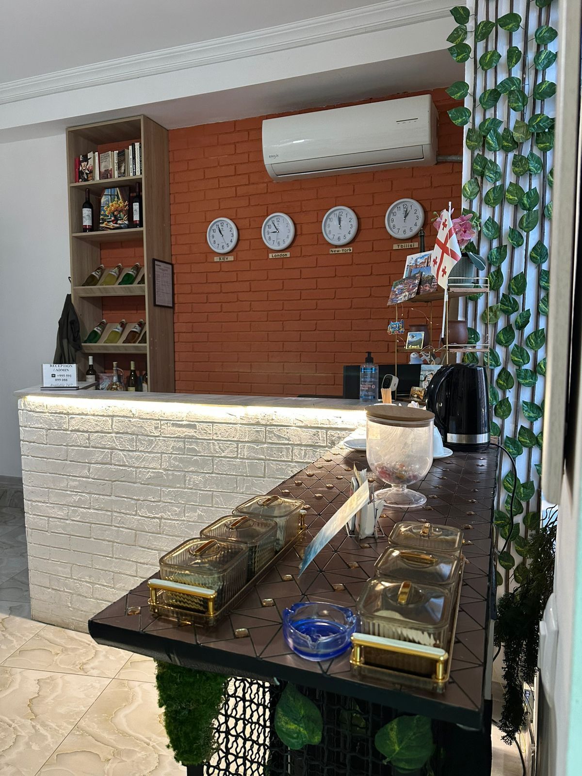 A reception area with a brick wall, clocks displaying different cities, a reception desk, and a bookshelf with books and wine bottles.