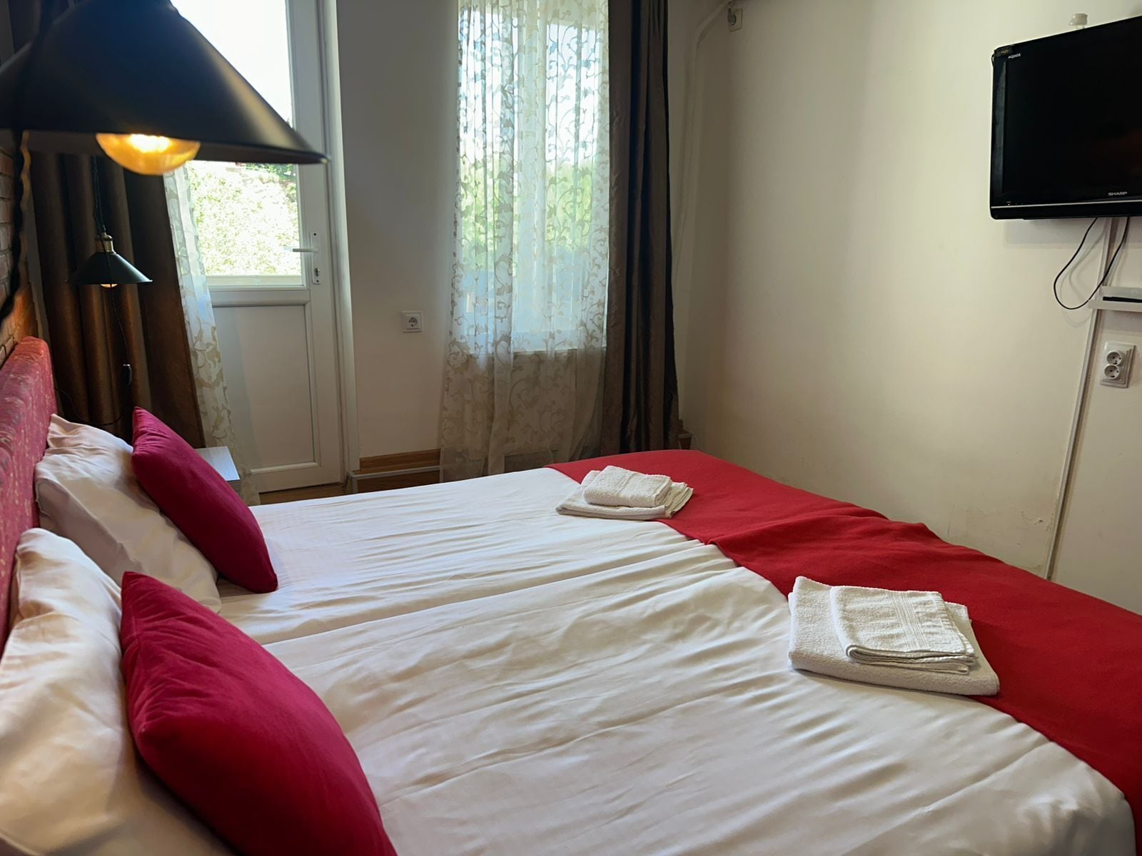 A hotel room with two beds, a TV mounted on the wall, and a window with curtains.