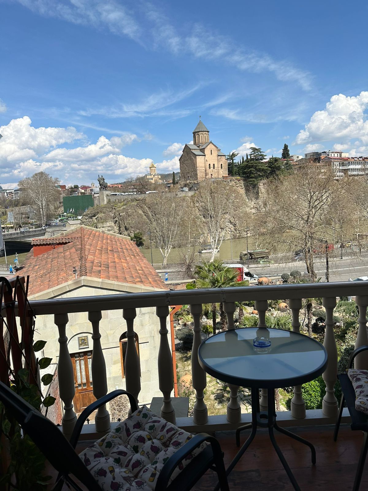 A balcony with a table and chairs, overlooking a cityscape with buildings and a church.