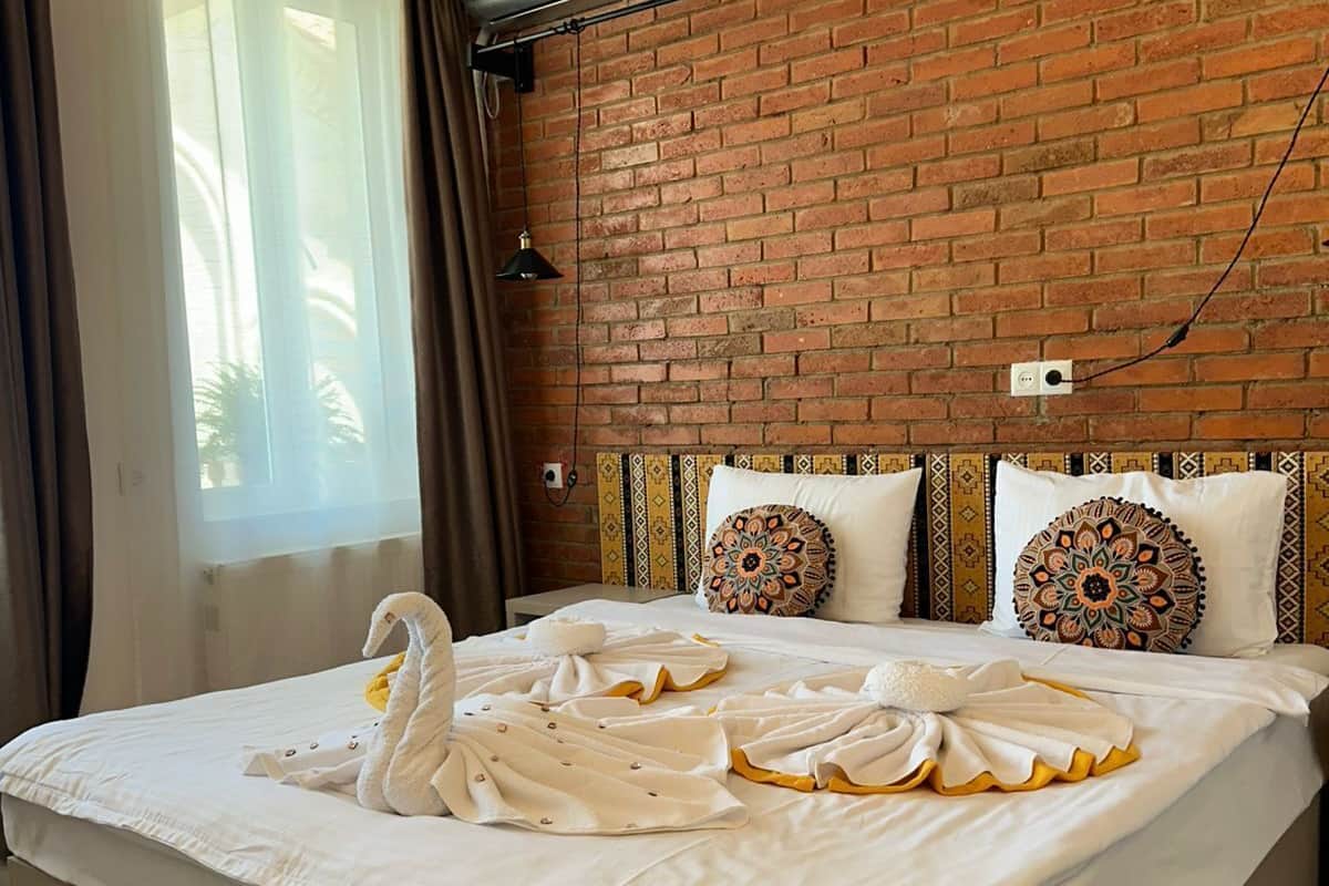 A hotel room with a brick wall, a bed with white bedding, decorative pillows, and a swan-shaped towel arrangement.