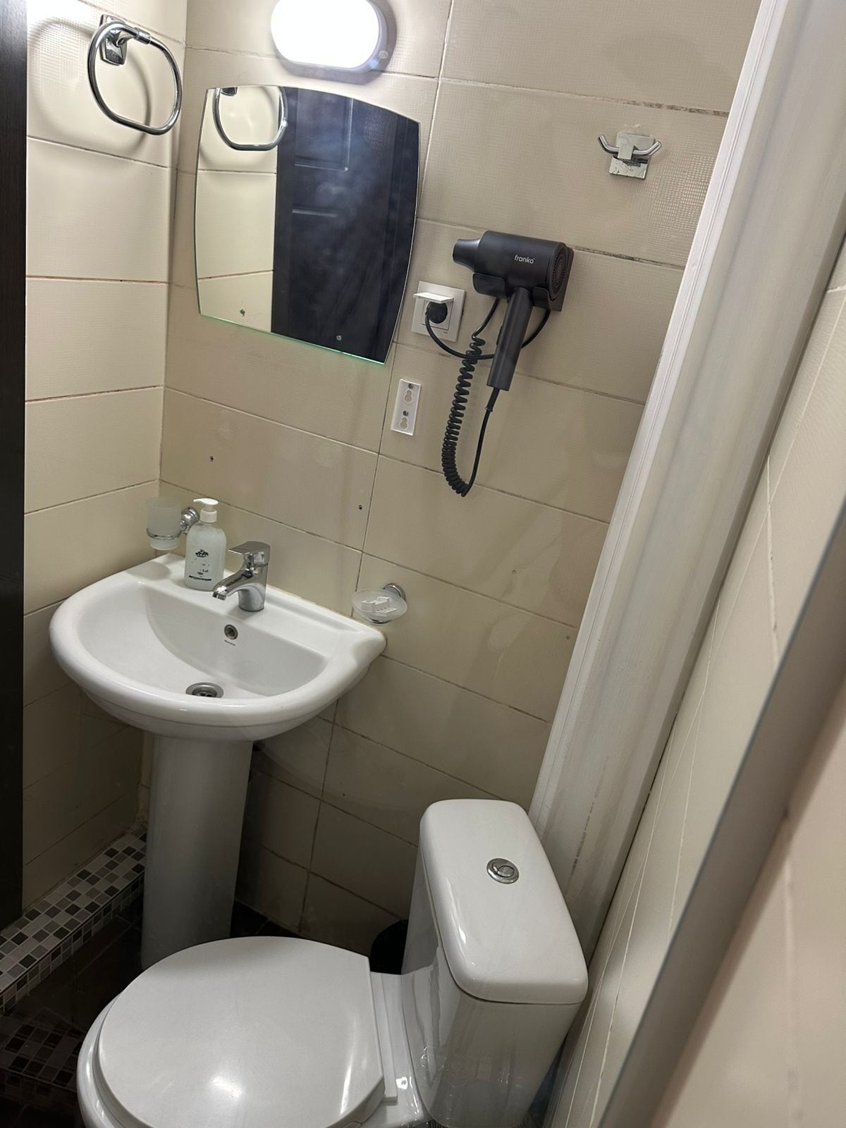 A bathroom with a white sink, a toilet, a mirror, and a hairdryer on a wall-mounted charging station.