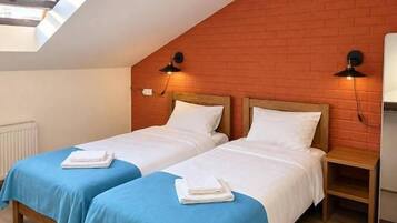 A room with two beds, a sloped ceiling, and a brick wall.