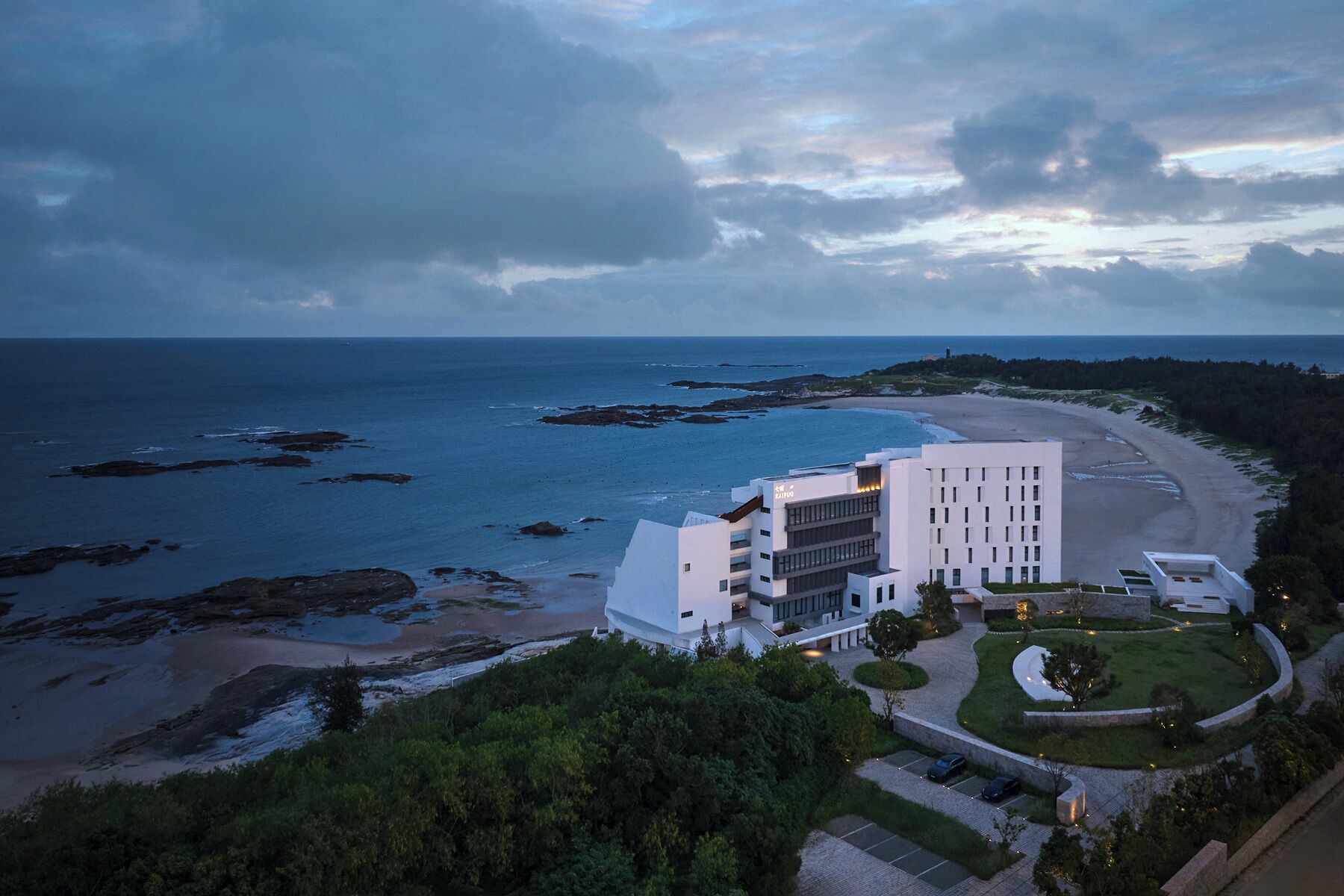 A coastal hotel with a modern design, featuring a central building with multiple floors and a landscaped garden.