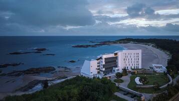A coastal hotel with a modern design, featuring a central building with multiple floors and a landscaped garden.