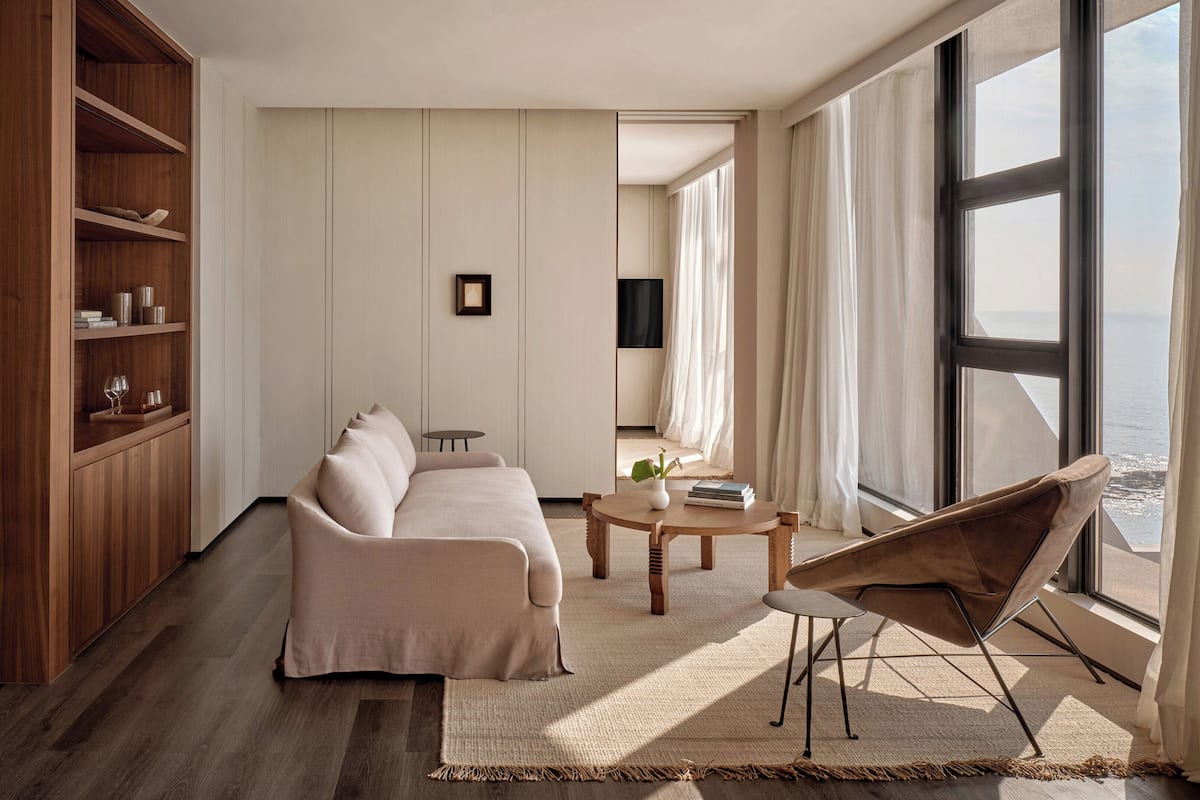 Un salon moderne avec un ensemble de canapés, une table basse et un téléviseur. Une grande fenêtre offre une vue sur l’océan.