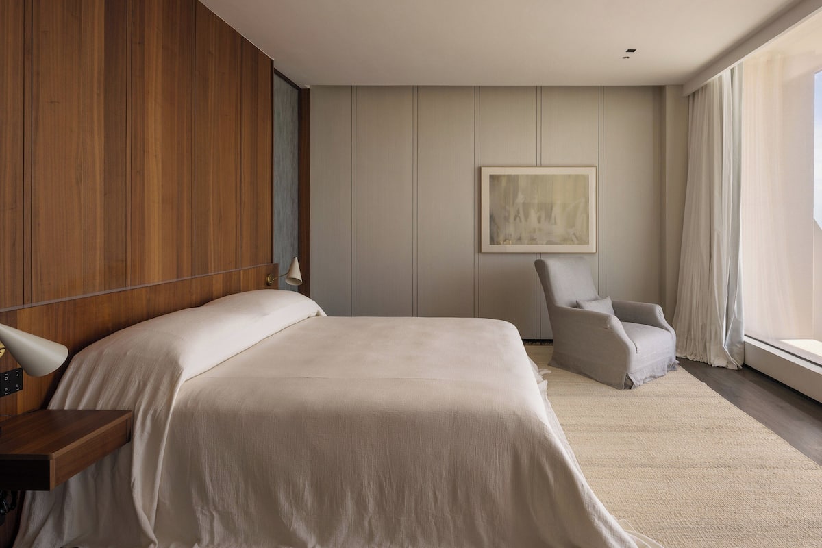 Une chambre d’hôtel moderne avec un grand lit, un fauteuil et une vue sur l’océan.