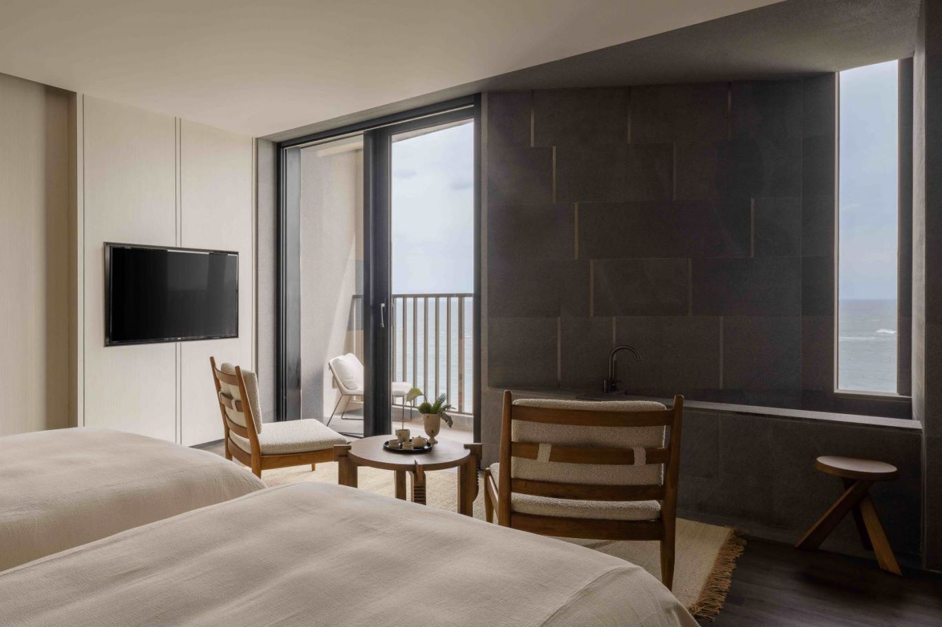 A hotel room with two beds, a TV, a balcony with a view, a small table with a chair, and a sink.